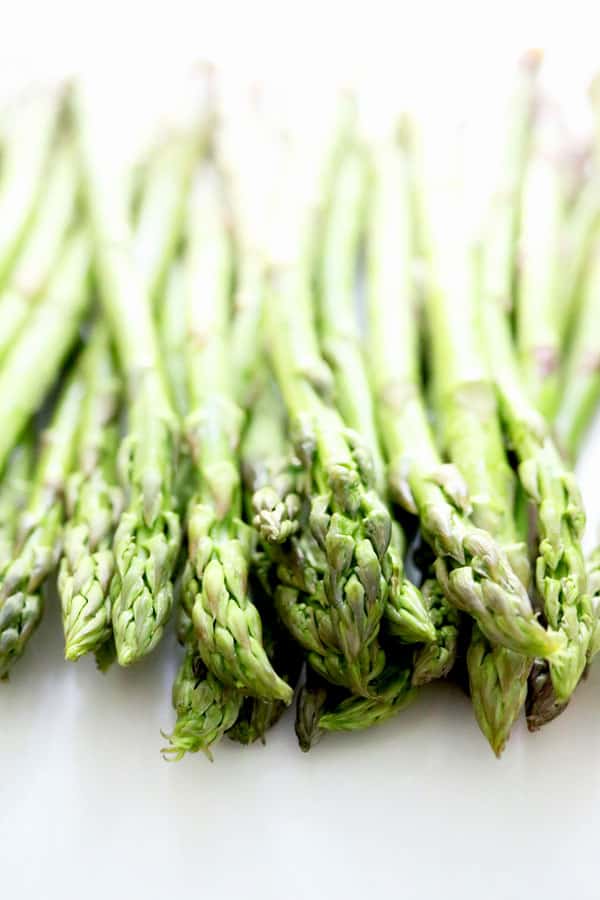 Pile of uncooked asparagus on a white surface. 