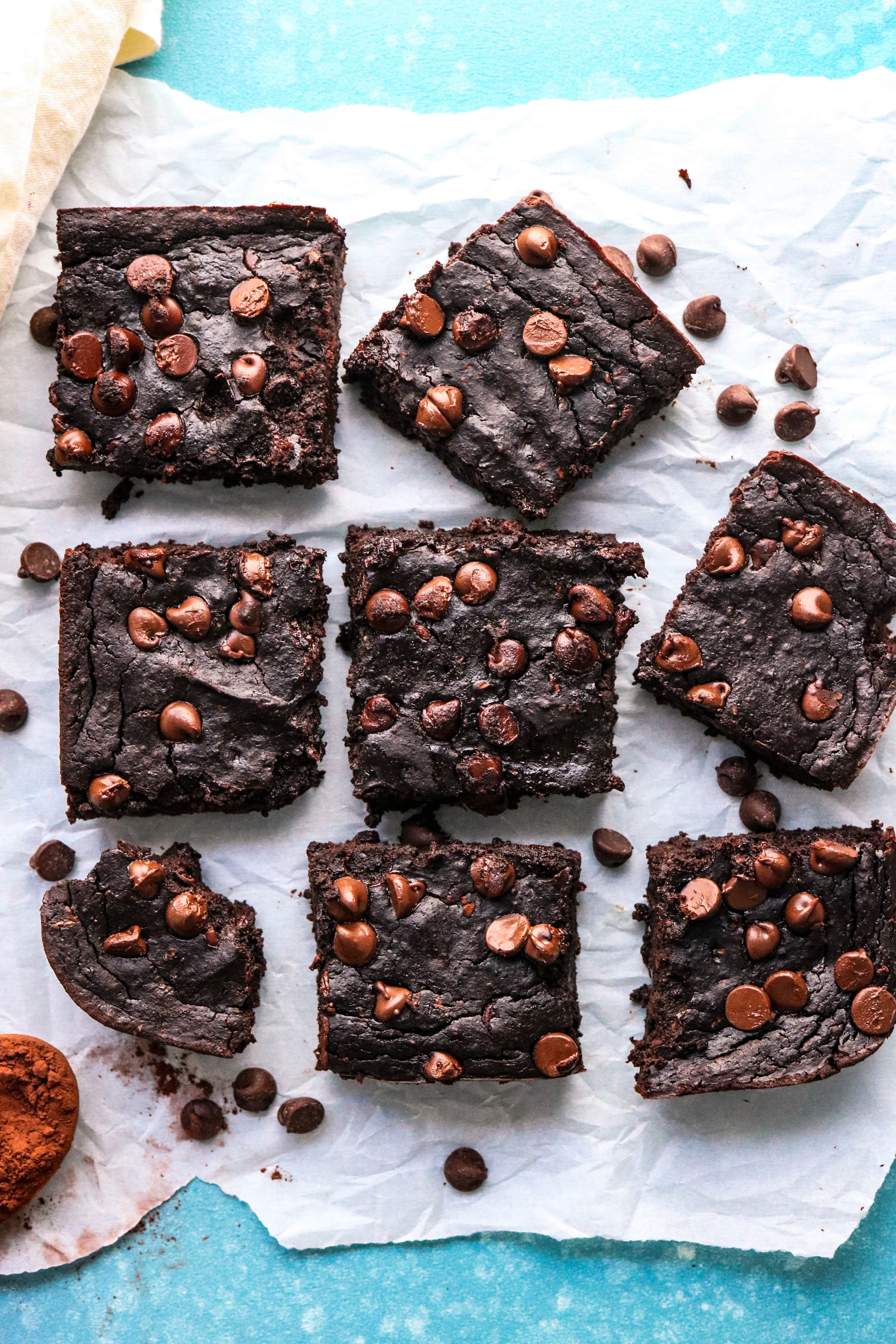 a few fudge brownies with chocolate chips on top, sliced and laying on top of parchment paper