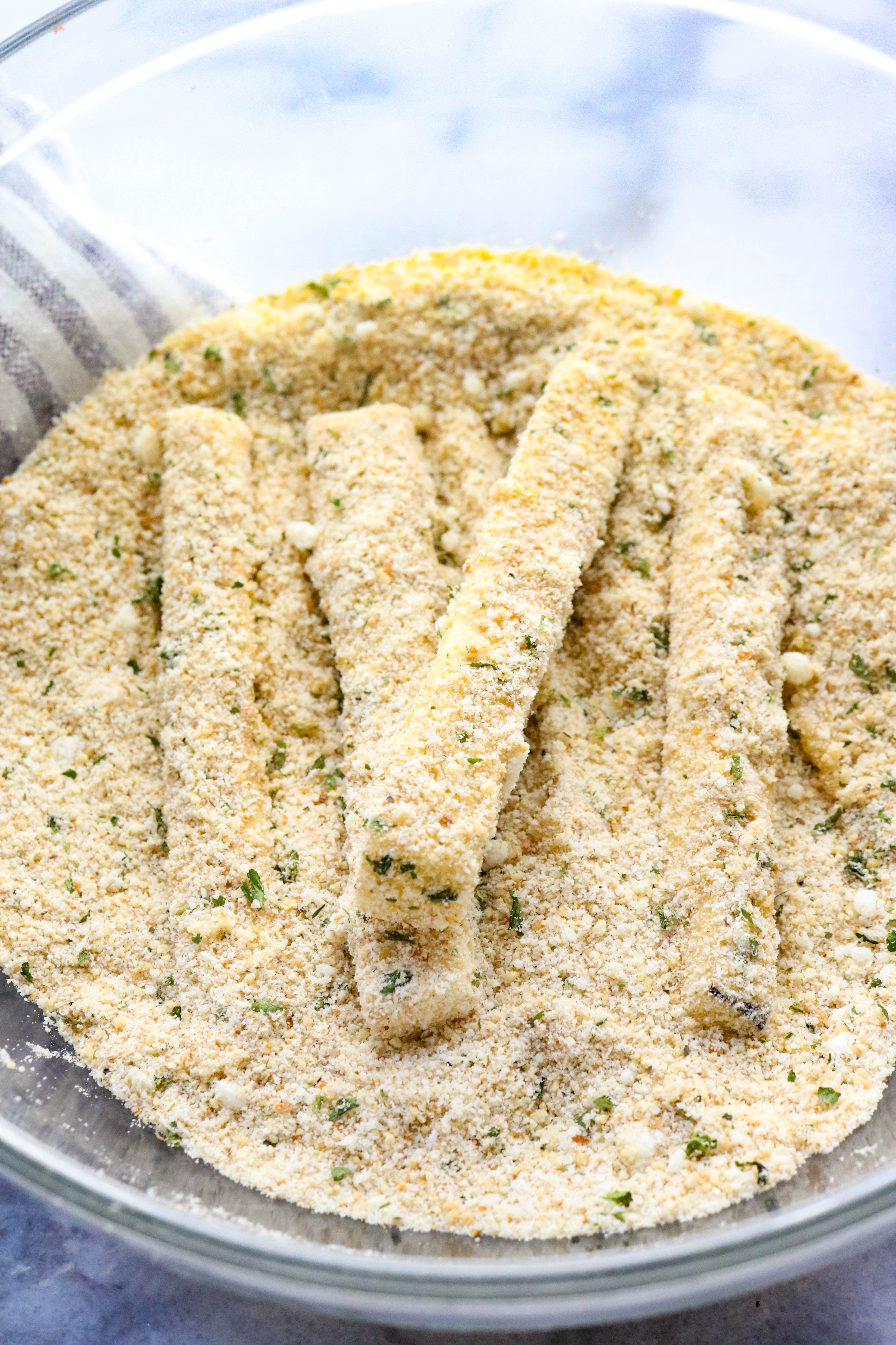 Eggplant sticks breaded laying in a bowl of seasoned breadcrumbs