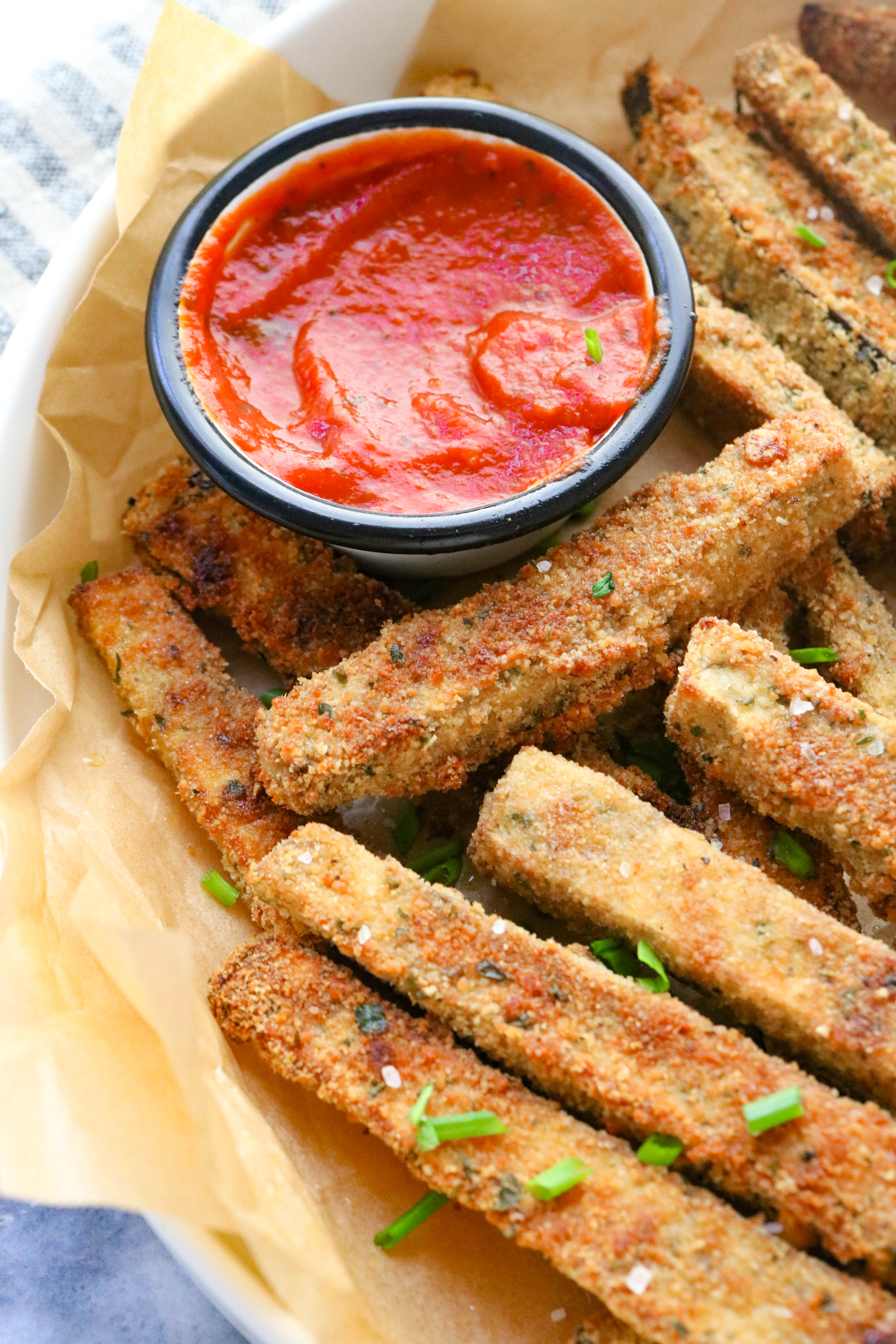 A pile of eggplant fries in a basket with red sauce d=next to it in a container. 