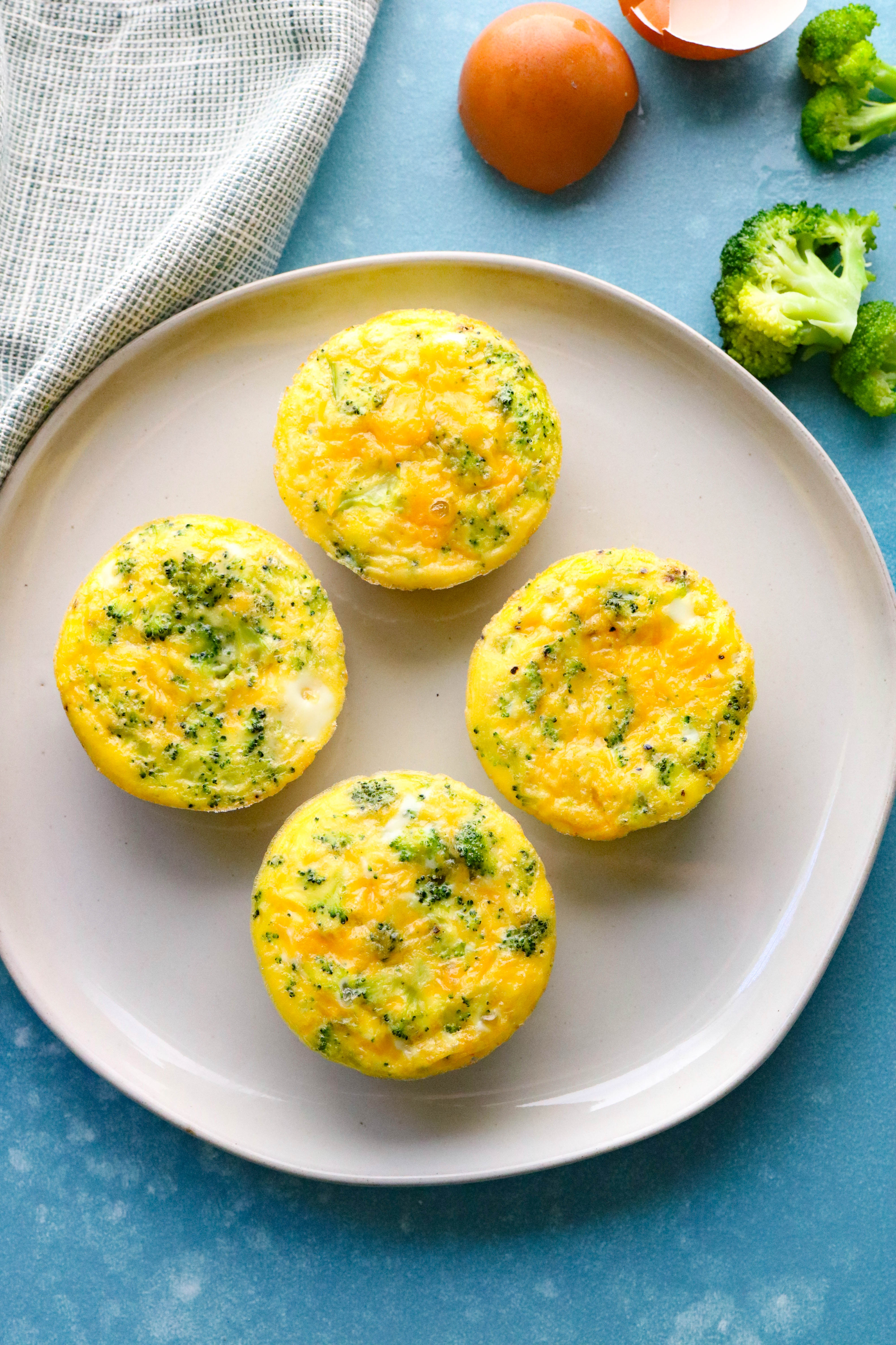 4 broccoli cheddar quiche cups on a plate with a blue background