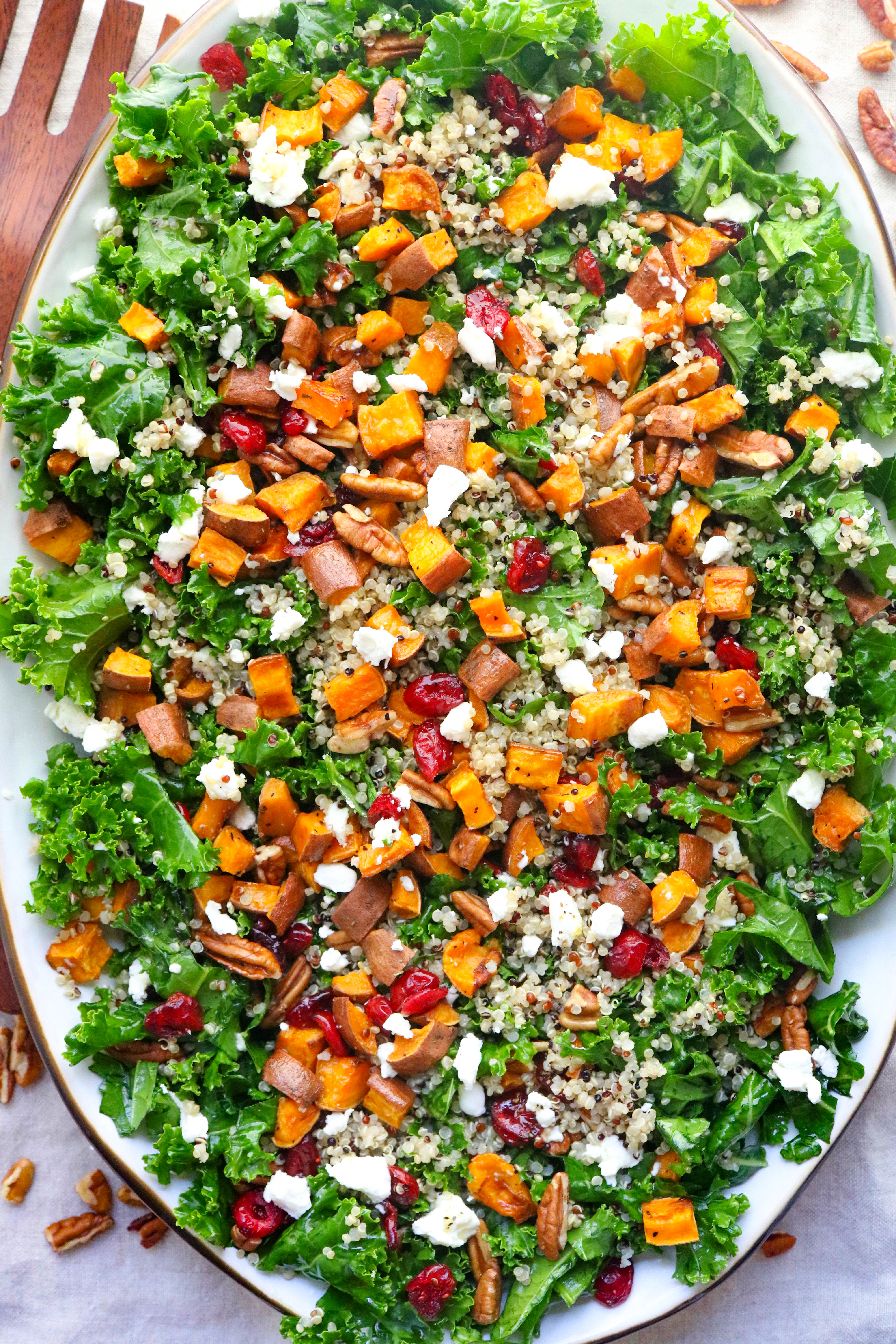 Oval platter filled with kale topped with notes, cranberries, goat cheese an roasted sweet potato. 