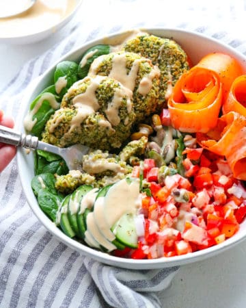 Healthy baked falafel in a bowl surrounded by veggies covered in tahini dressing