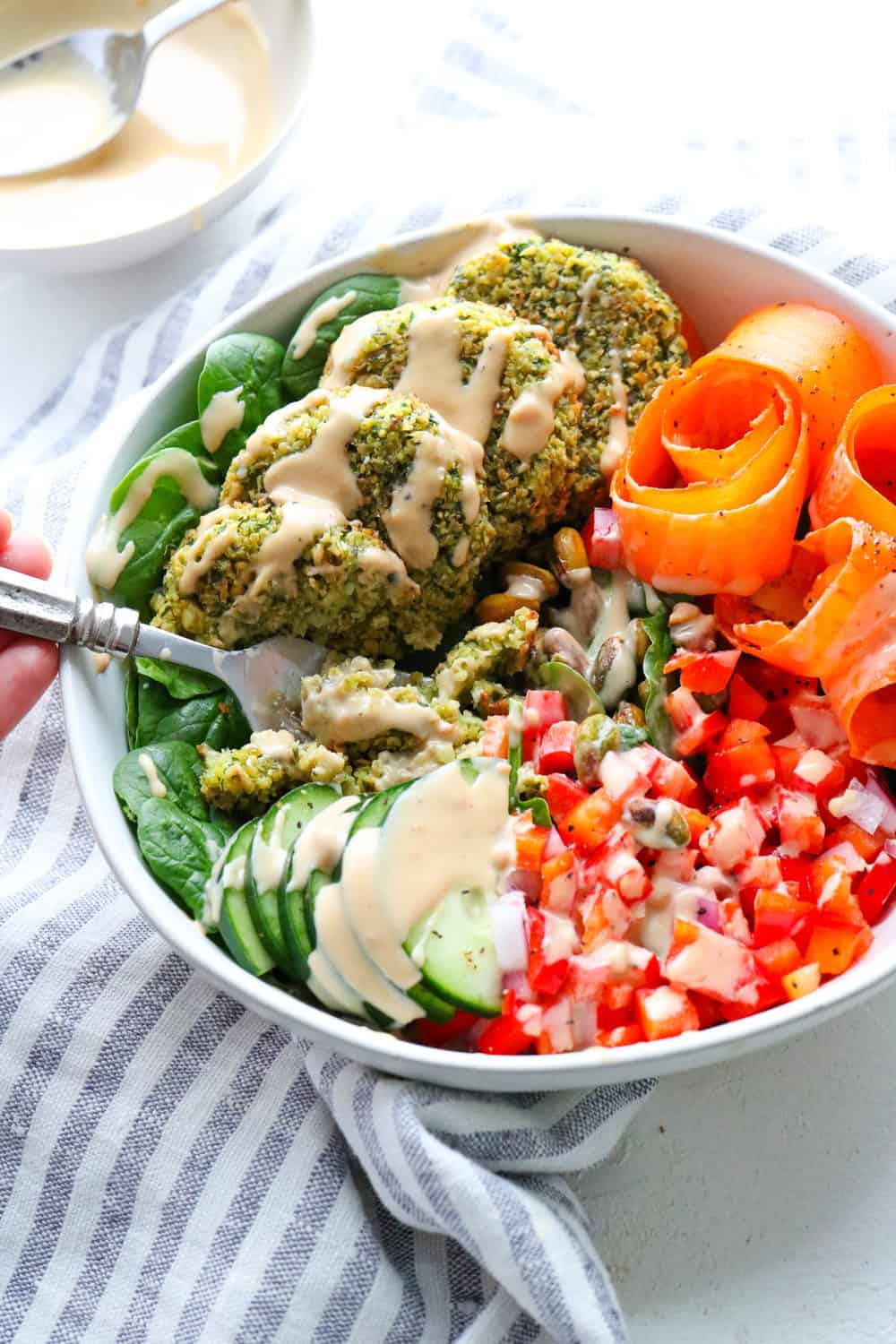 Healthy baked falafel in a bowl surrounded by veggies covered in tahini dressing