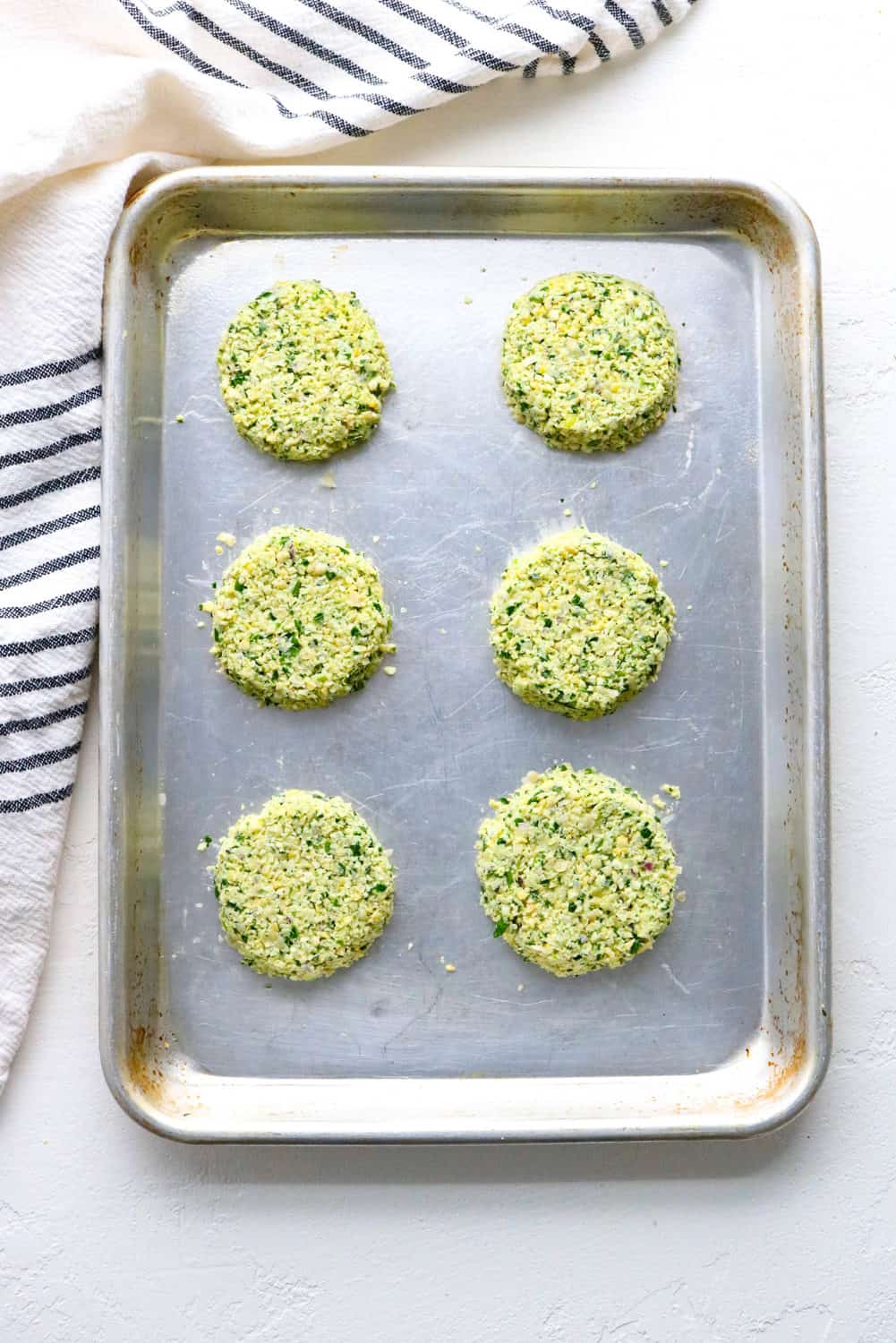 formed falafel patties on a baking sheet with a striped linen next to it