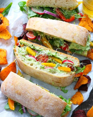 Slices of veggies sandwhich ontop of white parchment paper with yellow and red chips surrounding it