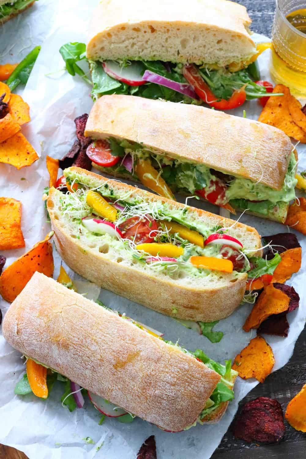 veggie sandwich sliced into portions on top of white parchment paper with veggie chips around it.