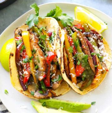 fajita veggies piled into charred corn tortillas with lime wedges next to it