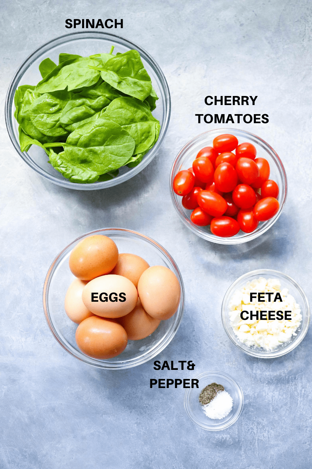 spinach in a round glass bowl with a bowl filled with cherry tomatoes next to it and a bowl of eggs in front of it. 
