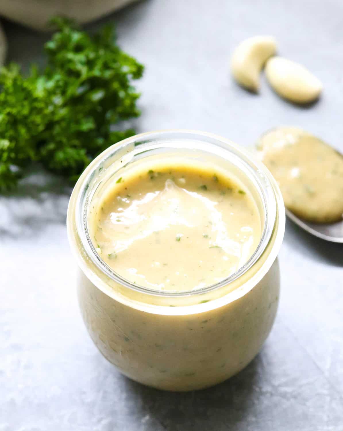 glass jar with creamy Caesar salad dressing in it with parsley behind it