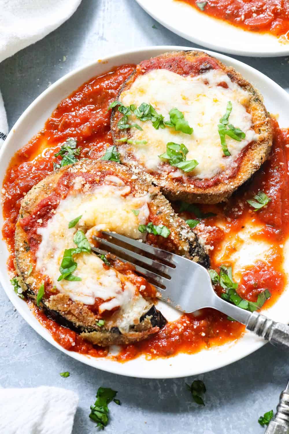 Sliced and coated healthy eggplant parmesan in tomato sauce and topped with melted cheese and chopped herbs