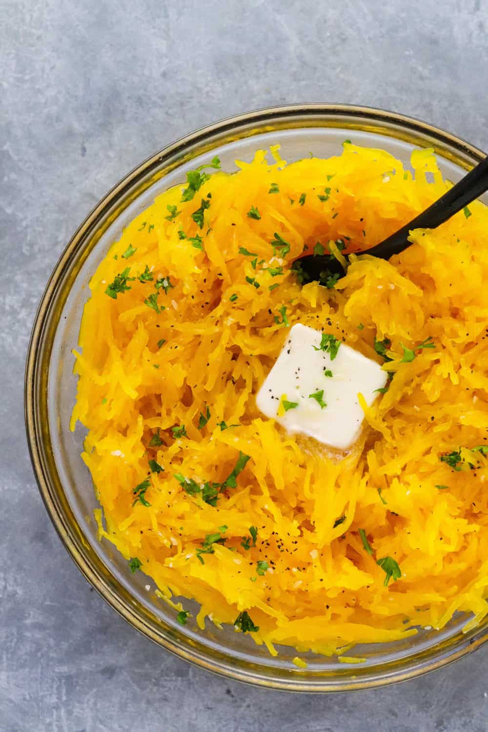 Bowl of instant pot spaghetti squash with a pat of butter on it with a black spoon in the bowl. 