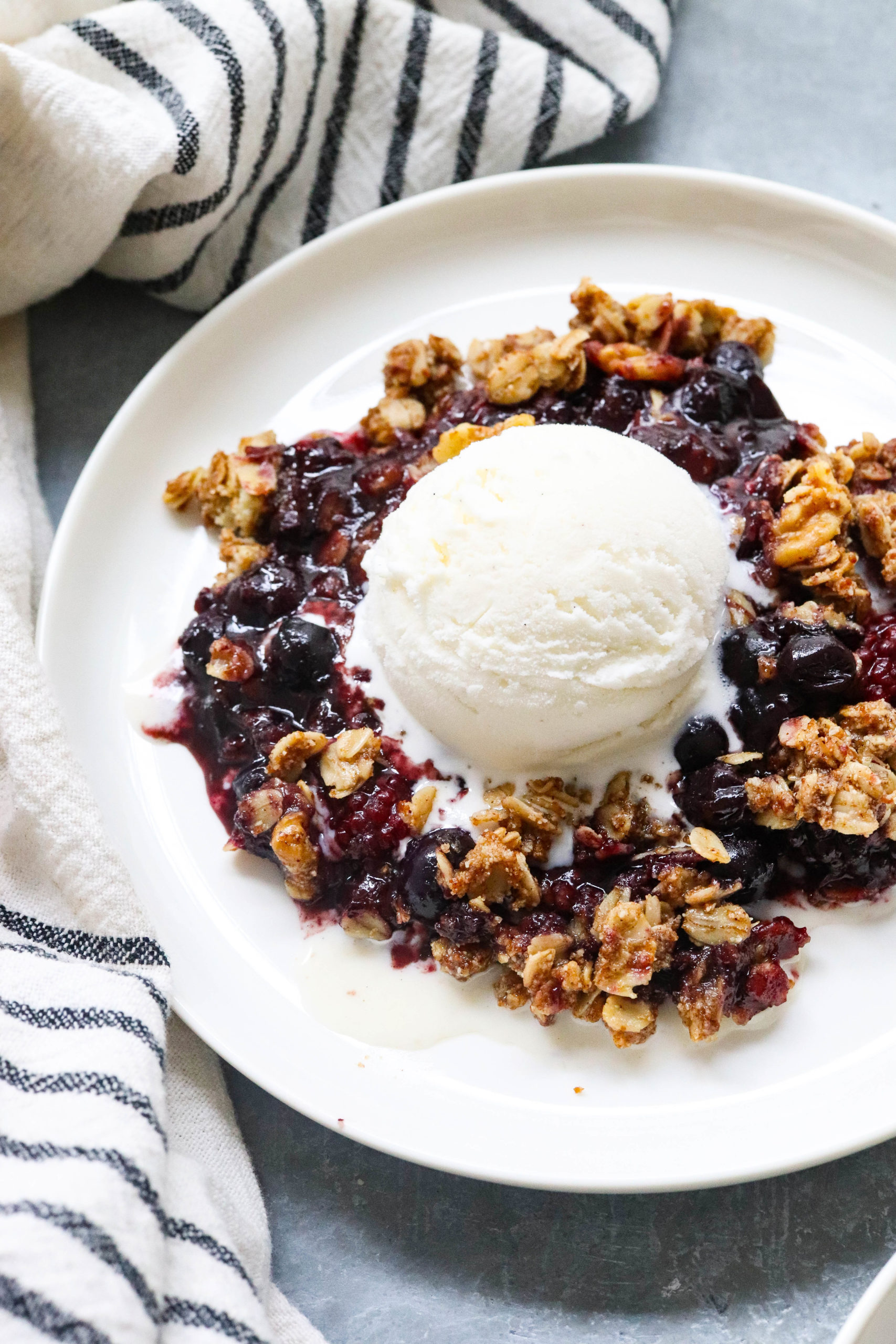 baked berry crisp on white plate topped with vanilla ice cream