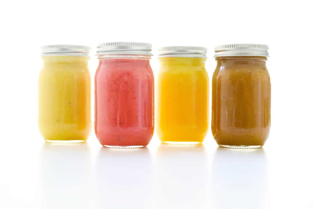 Four salad dressings in mason jars lined up next to one another