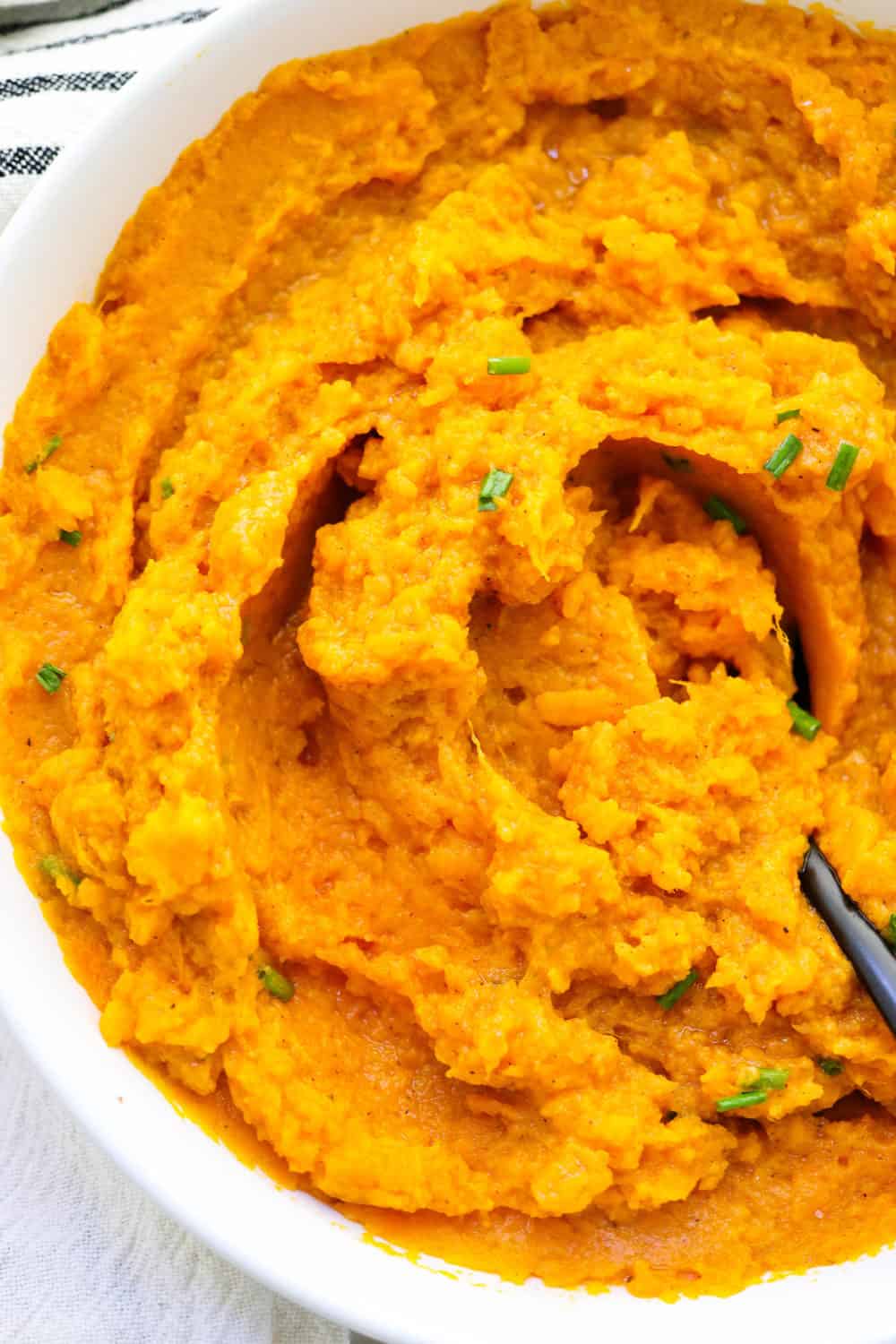 Spoon in a pile of fluffy mashed sweet potatoes with chives sprinkled on top of them. 