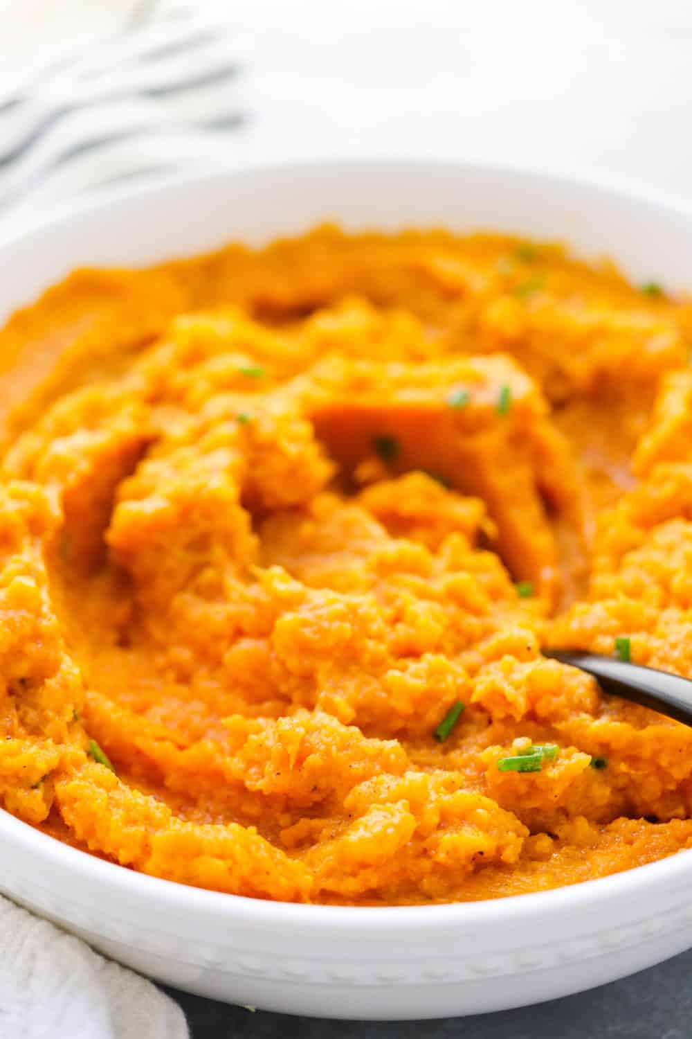 Close up of super fluffy sweet potatoes, mashed up in a serving bowl with a black spoon in the bowl of potatoes. 