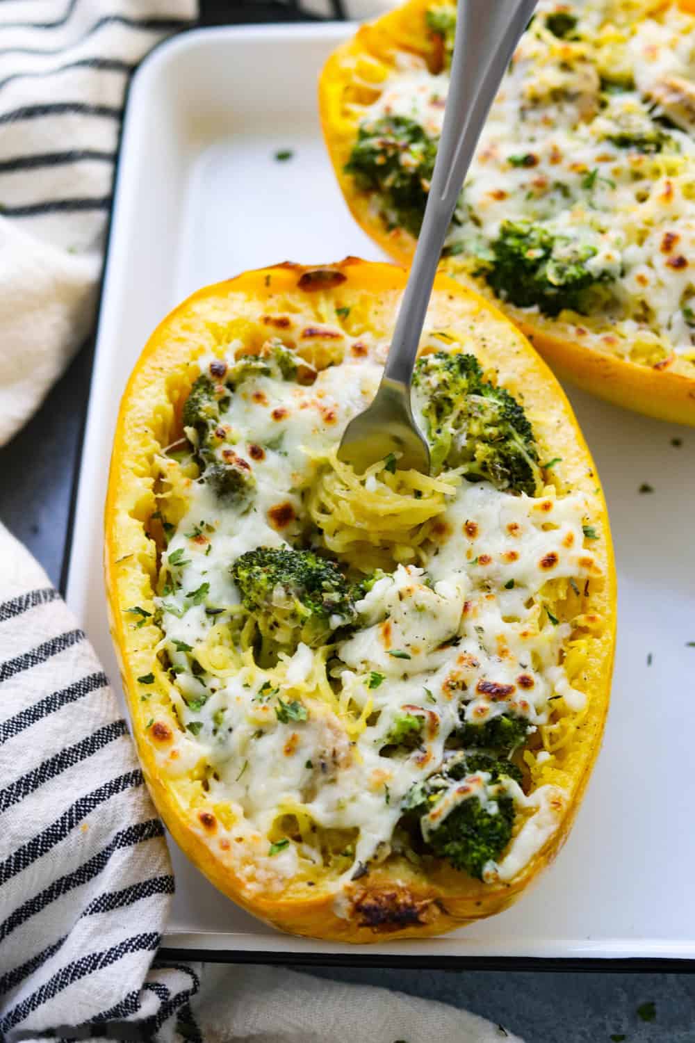 two halves of squash on a baking sheet with broccoli filling and melted cheese with a fork stuck in one.