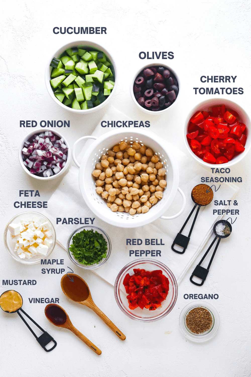 chickpeas, diced cucumber, cherry tomatoes, feta cheese, dressing ingredients, and diced red onion on a white surface