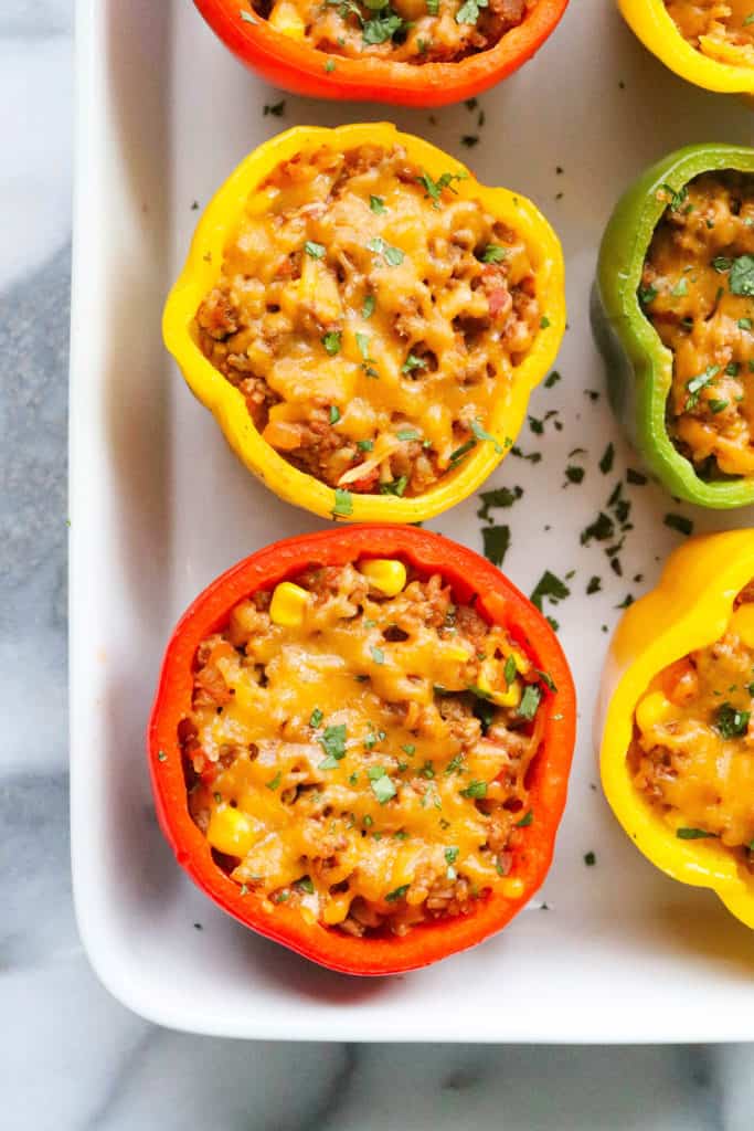 Baked stuffed bell peppers topped with melty cheese in a white baking dish. 