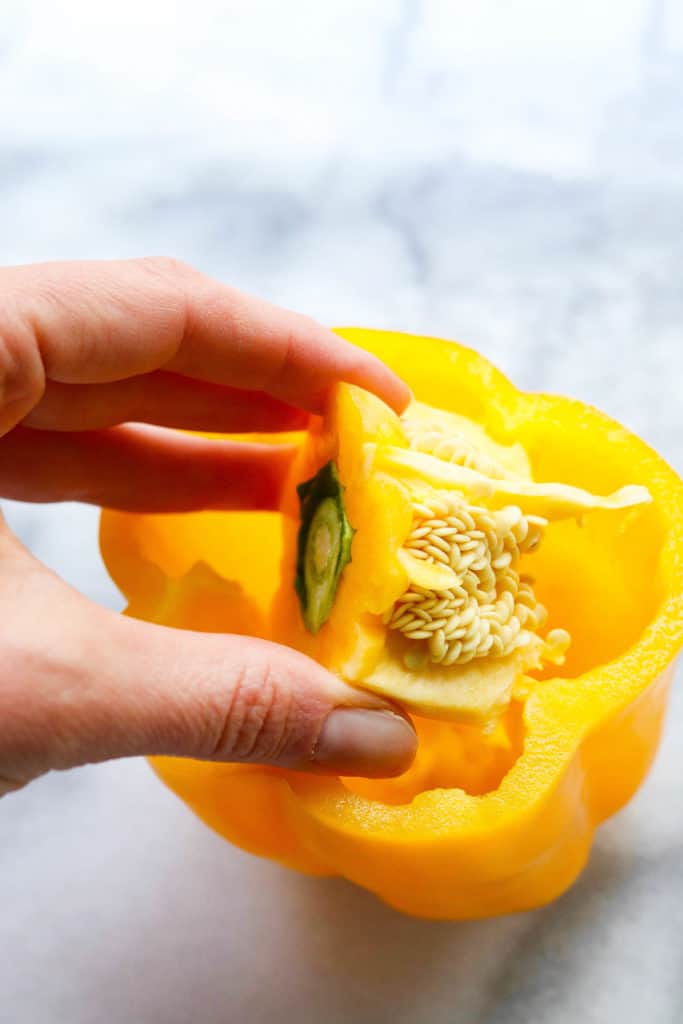 Hand pulling out the center of a yellow bell pepper. 