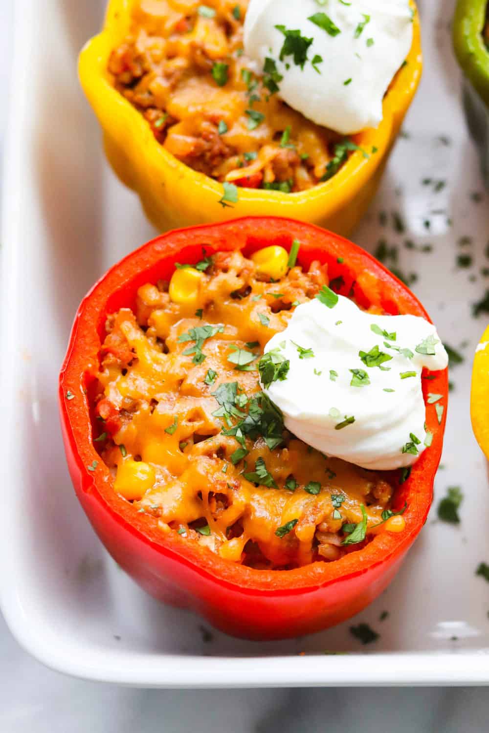 Taco stuffed pepper topped with melted cheese, sour cream and herbs in a white baking dish. 