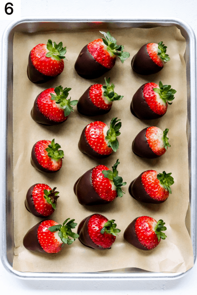 Tray with brown parchment paper on it filled with a few rows of dark chocolate covered strawberries. 