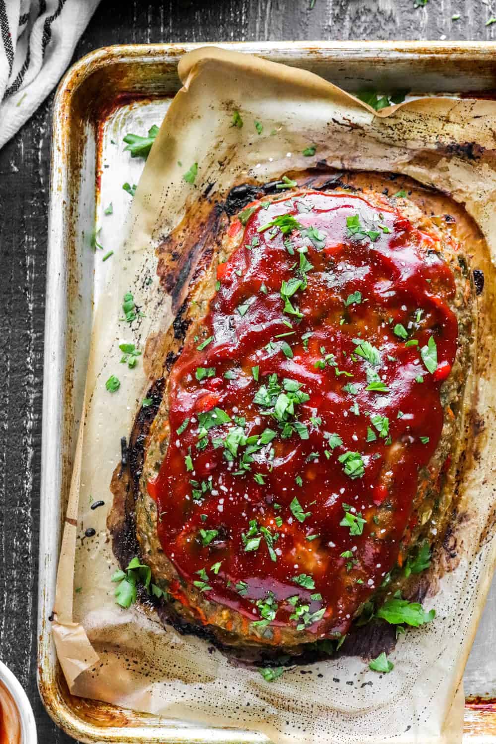 Whole baked meatloaf topped with red sauce and herbs on a baking sheet