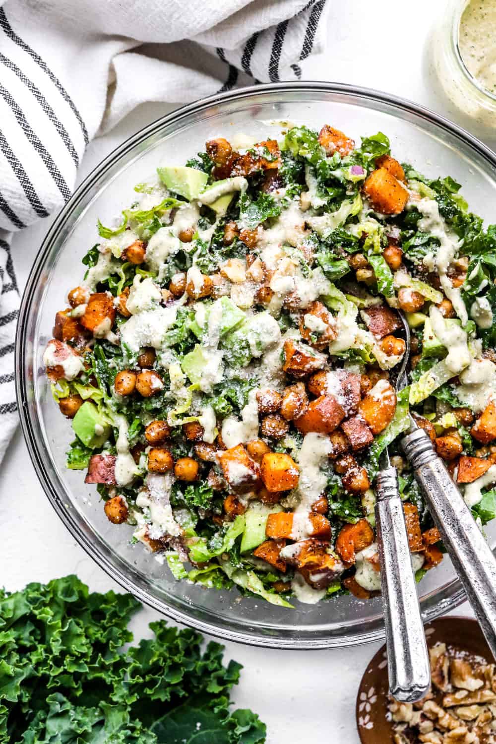 kale green salad in a glass bowl with chickpeas and sweet potato topped with creamy dressing