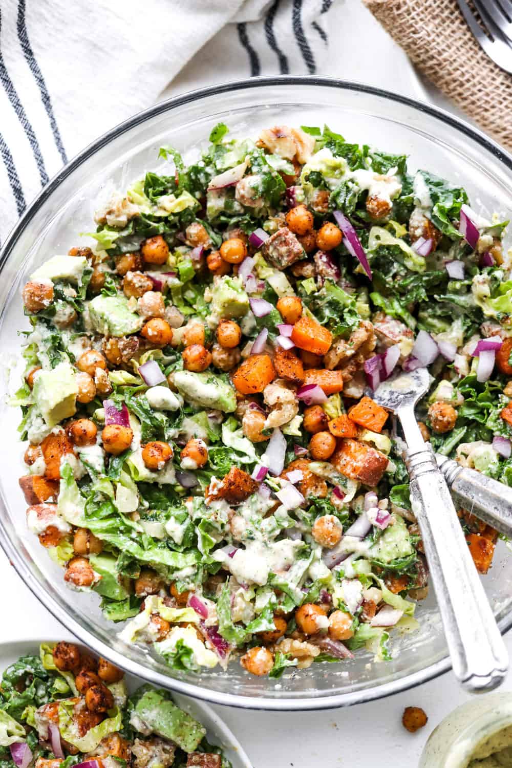 creamy kale Caesar salad mix with chickpeas and sweet potato in a large bowl with serving utensils in it. 