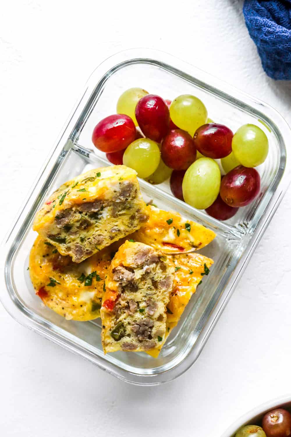 glass container filled with sausage breakfast egg muffins and multi coloured grapes