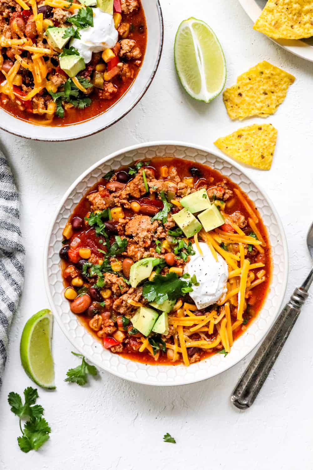 two bowls of red turkey chili on a white table with chips and limes next to it. 