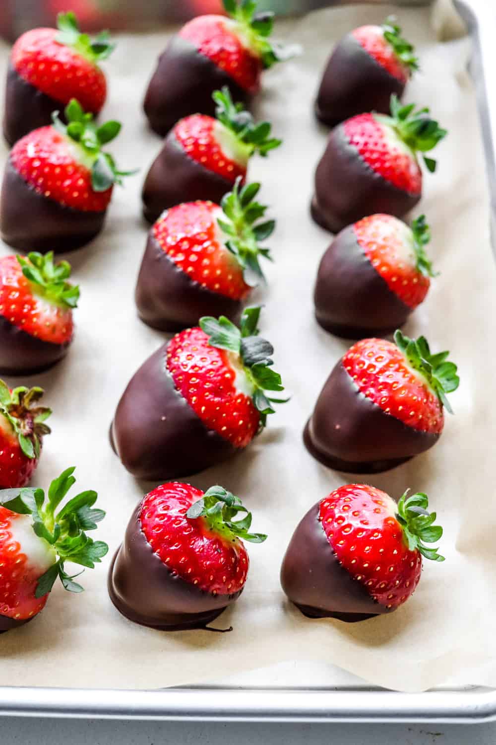 Tray filled with rows of dark chocolate covered strawberries on top of brown parchment paper. 