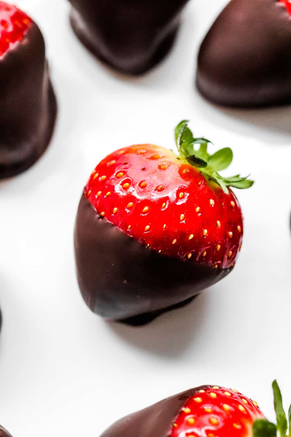 Close up of a single strawberry that has been dipped in chocolate with a few more behind it. 