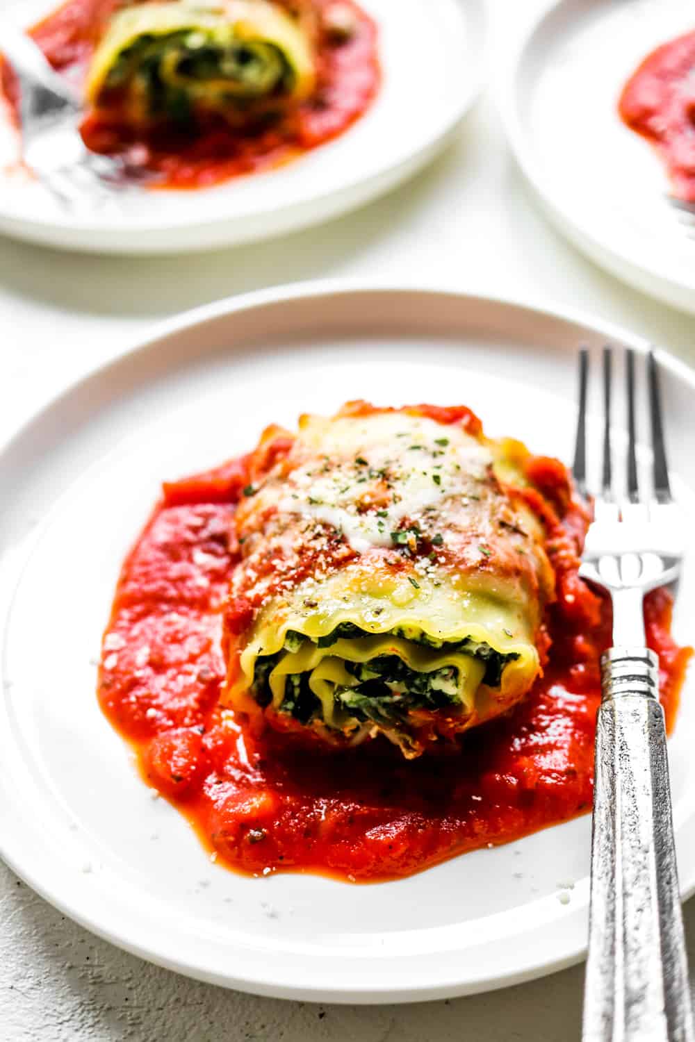 Straight on shot of spinach lasagna roll up with red sauce and melty cheese on top