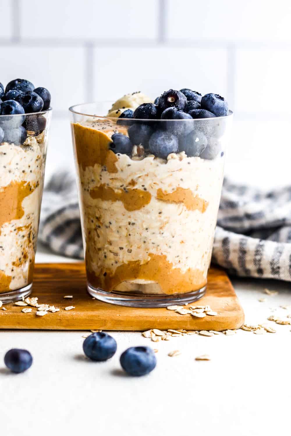 Glass cup filled with creamy oats, peanut butter and topped with bananas and blueberries