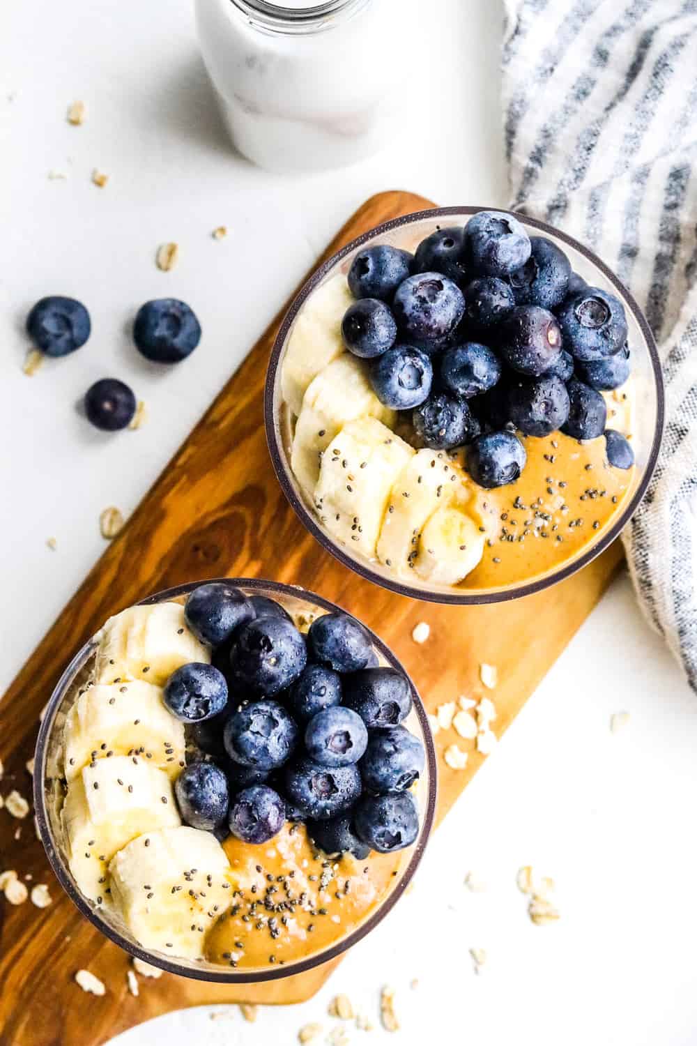 top view of cups of overnight oats topped with blueberries and banana on a wooden board