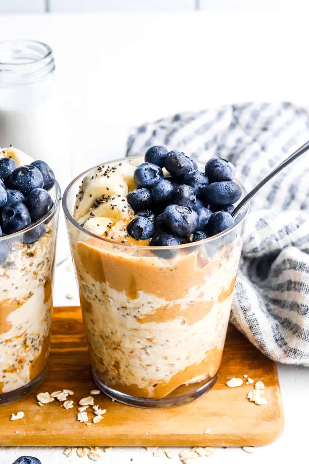 cereal in a cup with a spoon in it filled with peanut butter and blueberries on top with another one next to it.