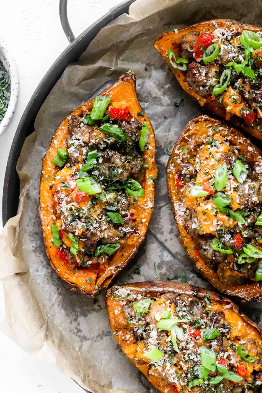 Tray of roasted twice-baked sweet potatoes filled with cooked ground sausage and peppers with grated cheese and green onion on top of them. 