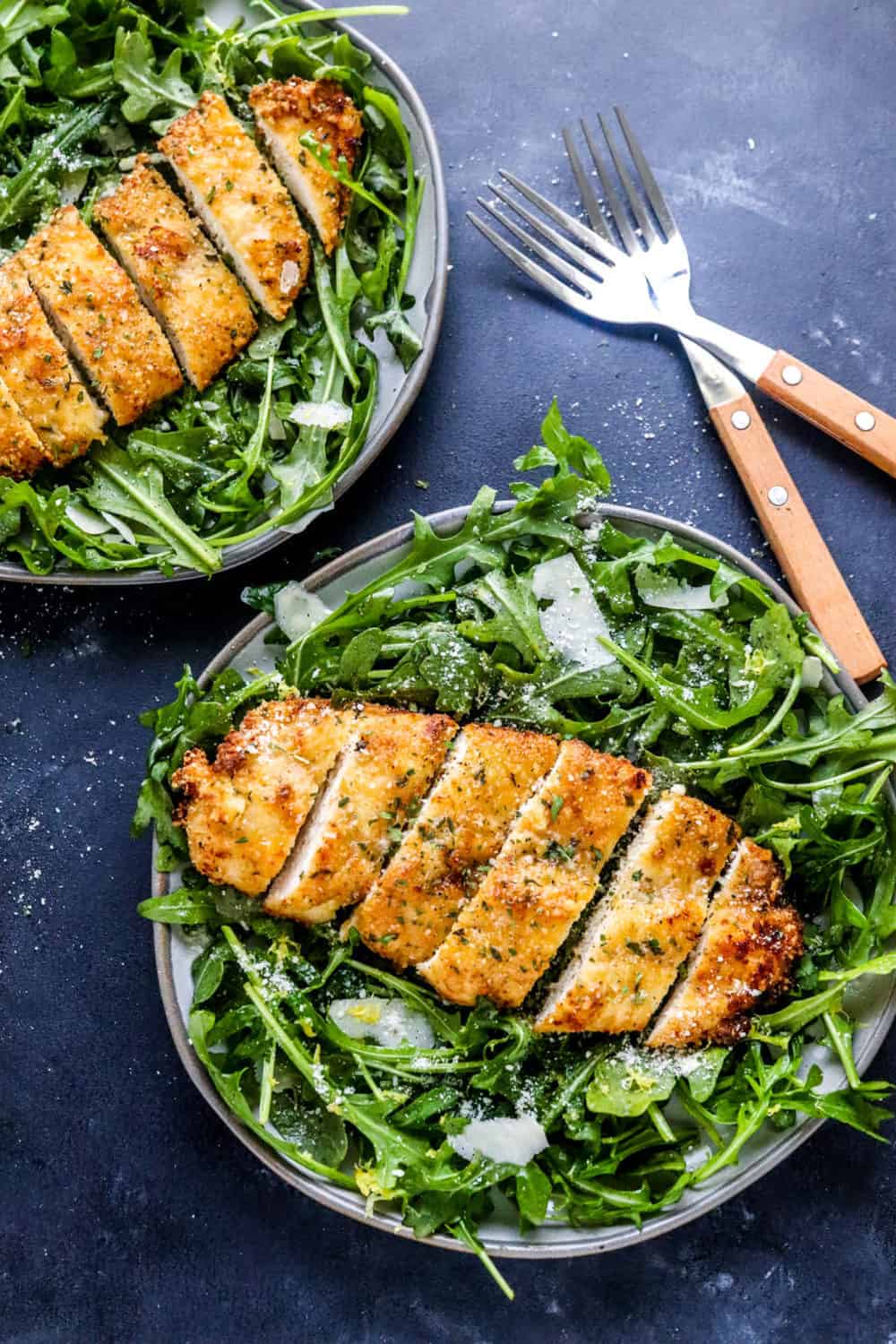 two grey plates filled with arugula salad topped with crispy breaded chicken breast
