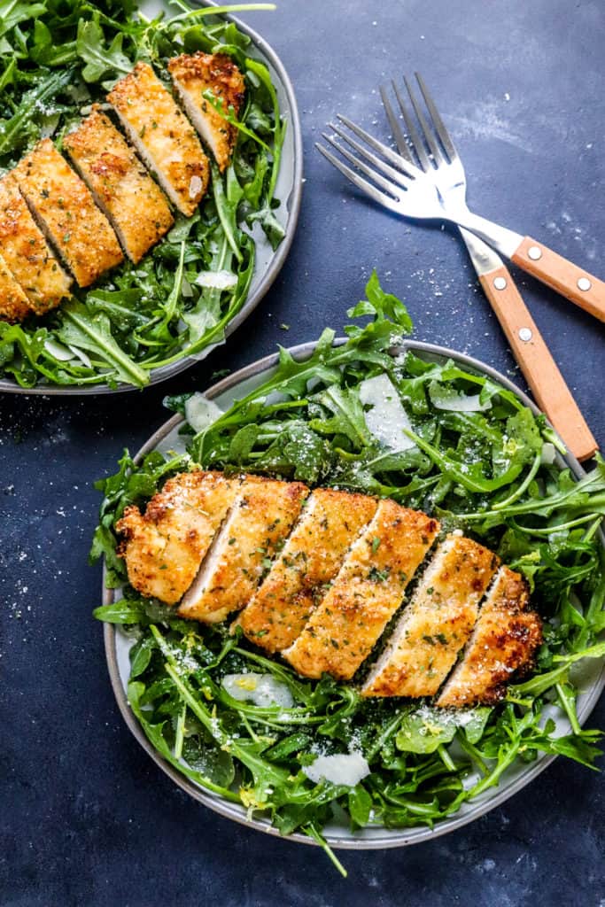 Top plates filled with greens topped with crispy chicken with two forks next to the plates. 