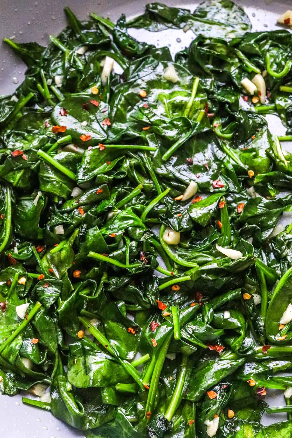 Wilted sautéed spinach with garlic in a pan topped with red pepper flakes