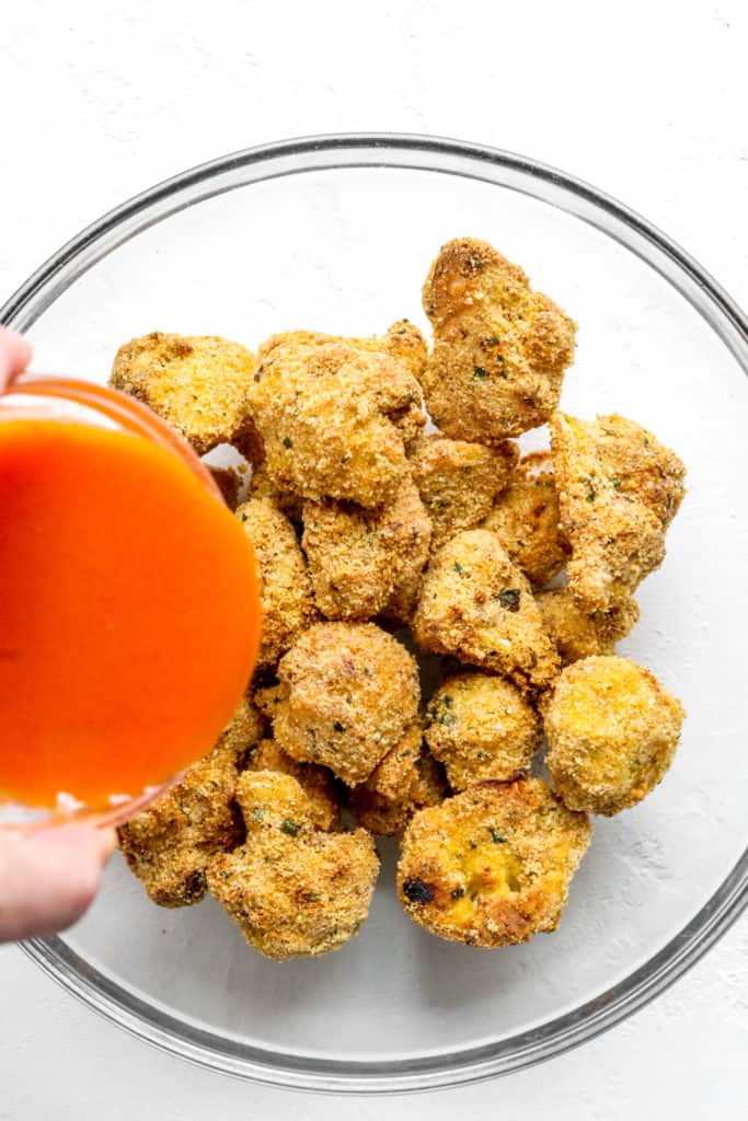 Pouring buffalo sauce over a bowl of breaded, cooked veggies. 