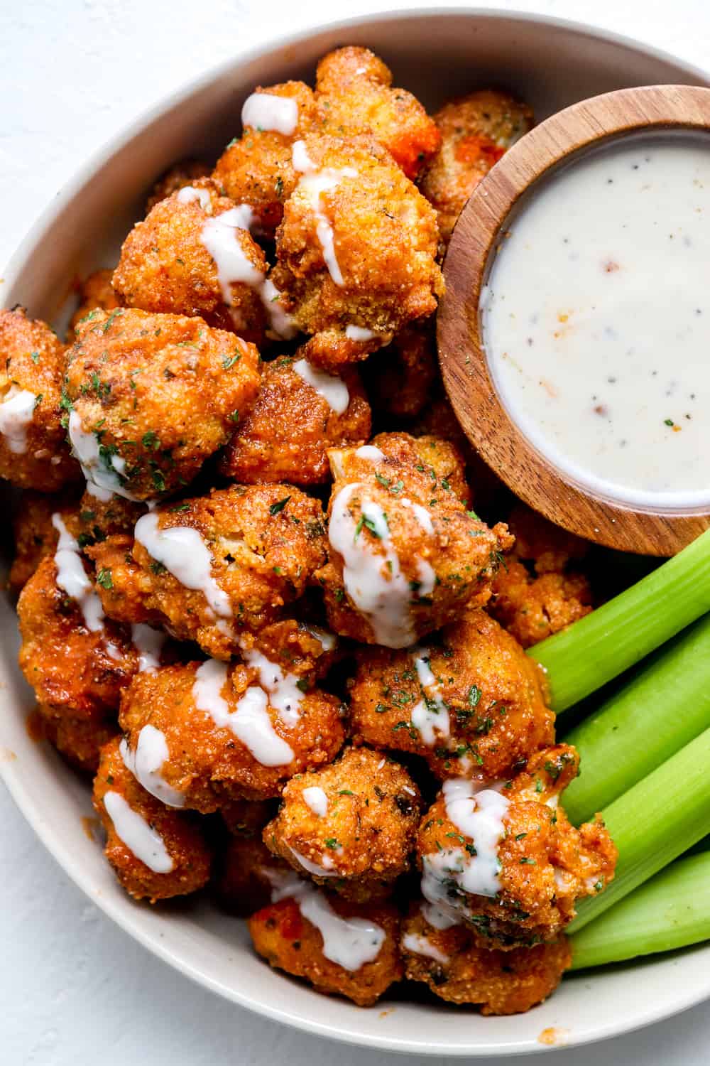 Crispy buffalo ari fryer cauliflower in a round white dish covered in a white sauce with celery sticks next to ti