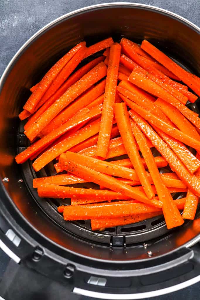 Uncooked carrot fries in the basket of an air fryer