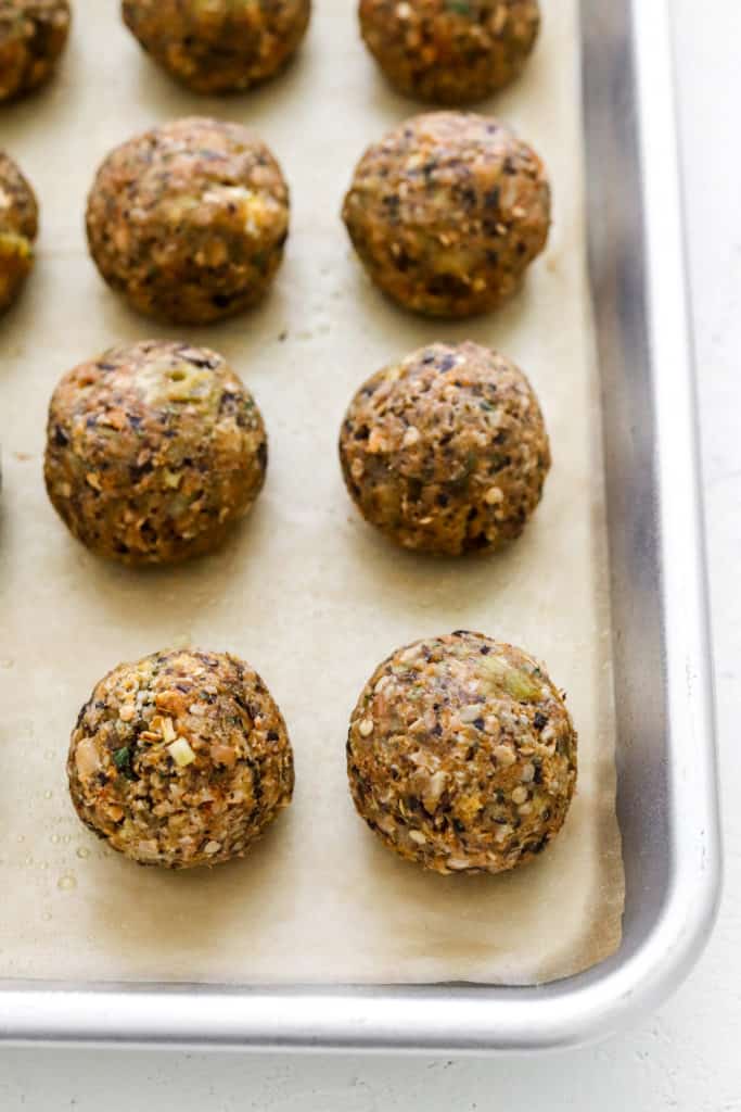 Golden brown baked vegetarian meatballs on a sheet pan on top of brown parchment paper.