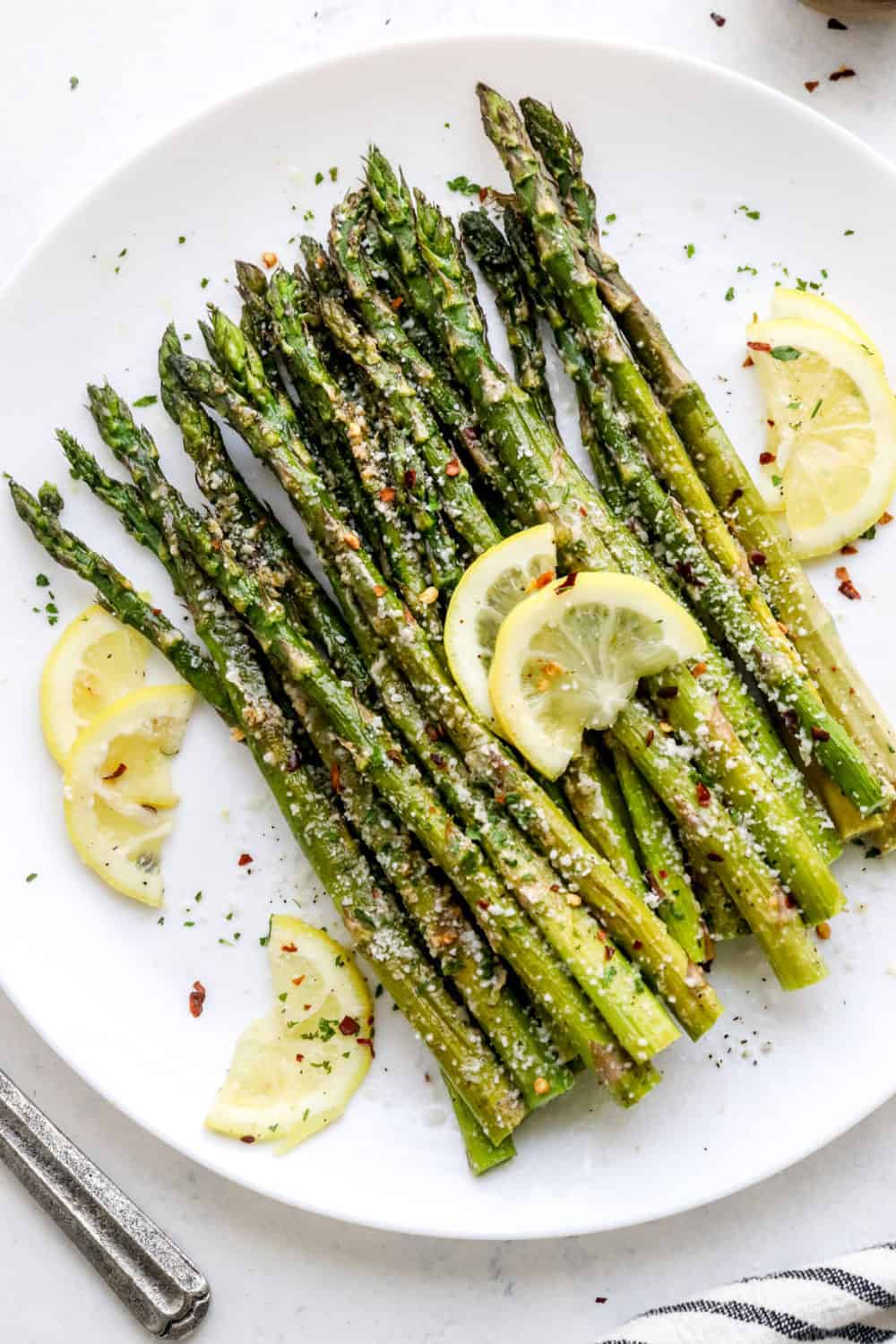 Cooked asparagus in a pile on a round white plate with sliced lemon laying on top of it