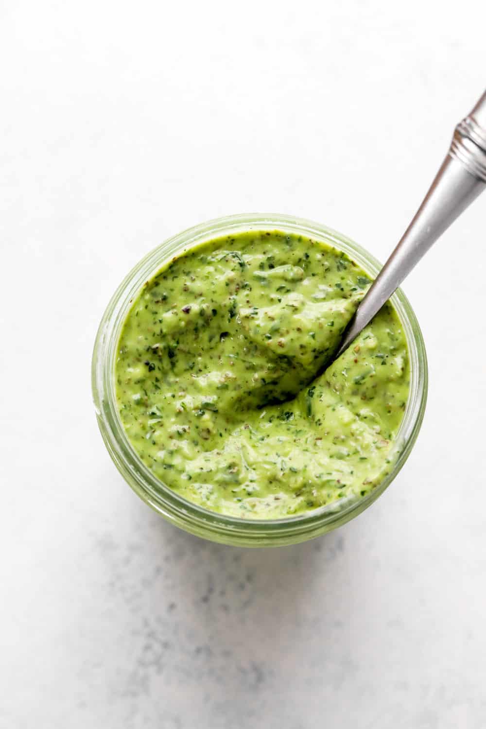 Green Goddess Dressing in mason jar with a spoon in it. 