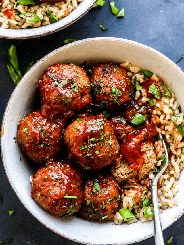 Turkey meatballs in a white round bowl covered in red sauce on top of brown rice with a fork in the bowl and another bowl of meatballs and rice behind it