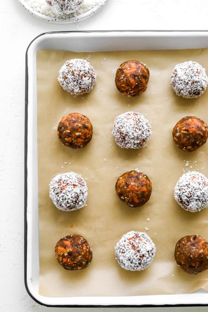 Carrot cake balls with some brown and some white in rows on  brown parchment paper