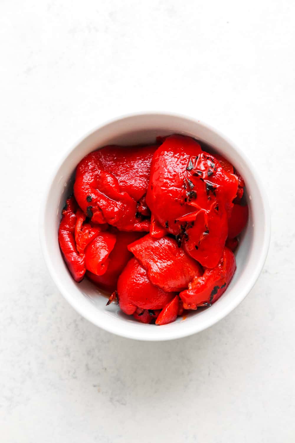 Roasted red peppers in a round white bowl on a white surface